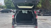 Rear view of a dark SUV with its tailgate raised, revealing a large open cargo area and folded rear seats in a parking lot.