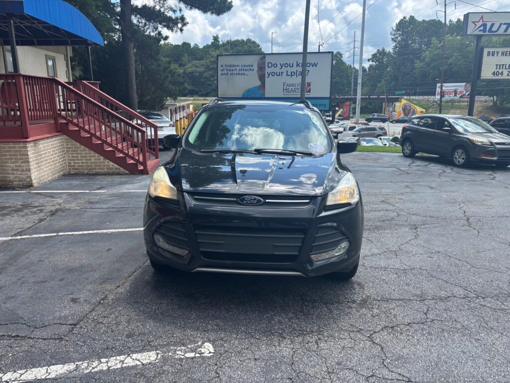 Front view of a black Ford SUV parked in a lot, with a red railing building on the left and billboards in the background. Was this helpful? Or should I tailor it to a specific page?