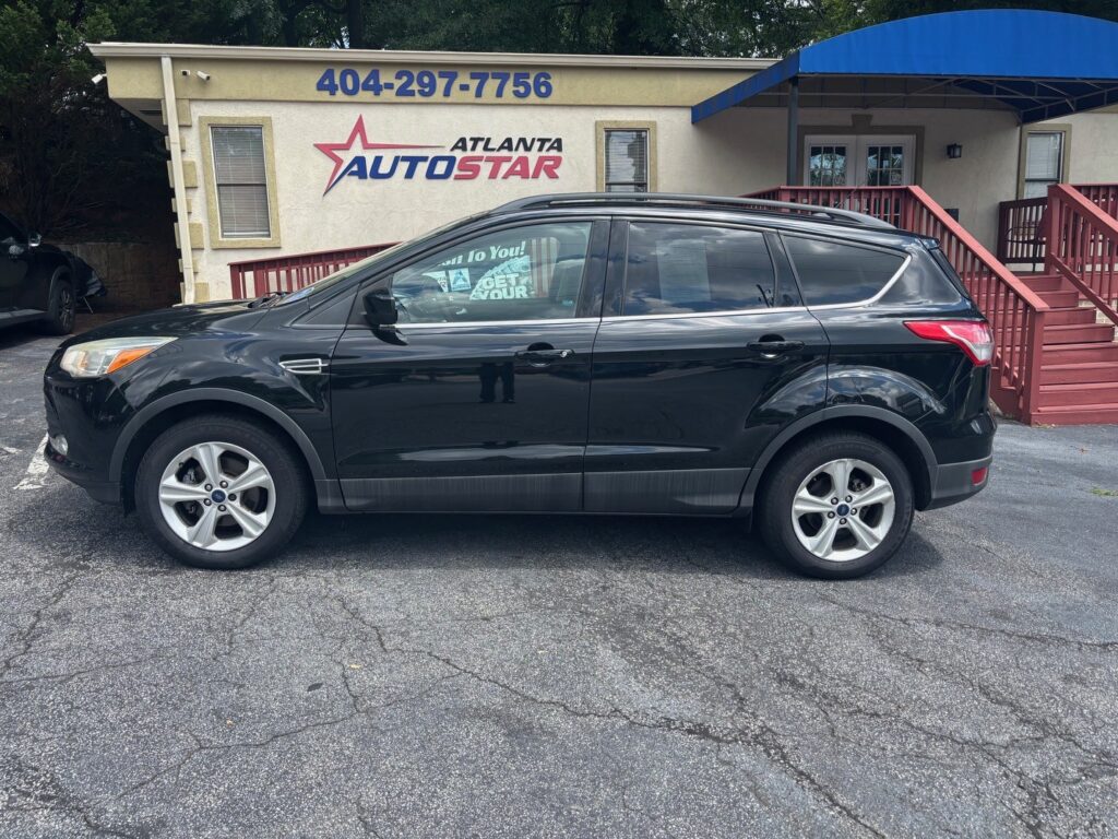 Black SUV parked in front of an Atlanta AutoStar dealership building with a sign and stairs to the right, blue awning overhead